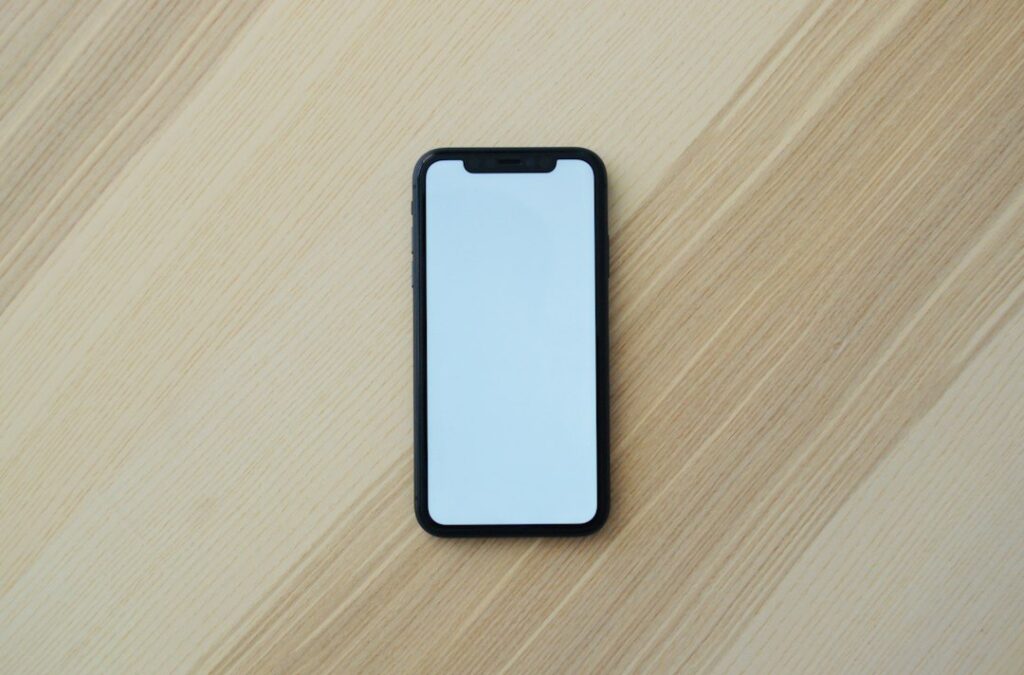 木のテーブルに置いた画面に情報のないスマートフォン
