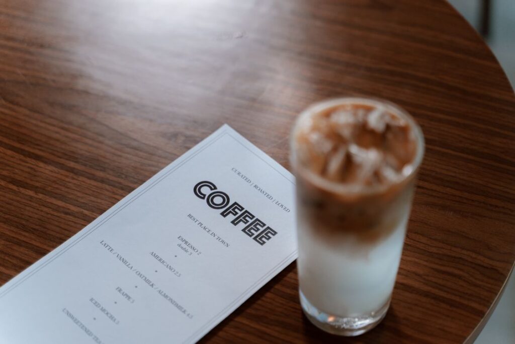 木のテーブルに置かれたコーヒーメニューとグラス入りの飲み物