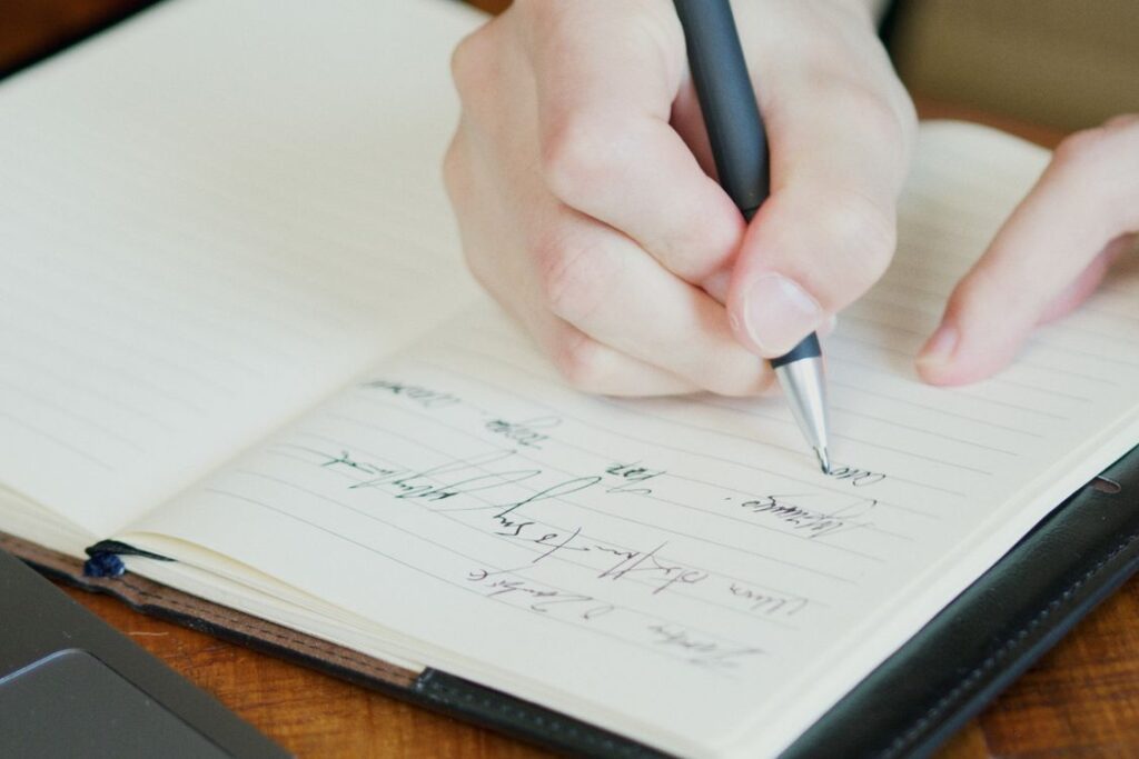 開いた罫線入りのノートにペンで書き留める手元