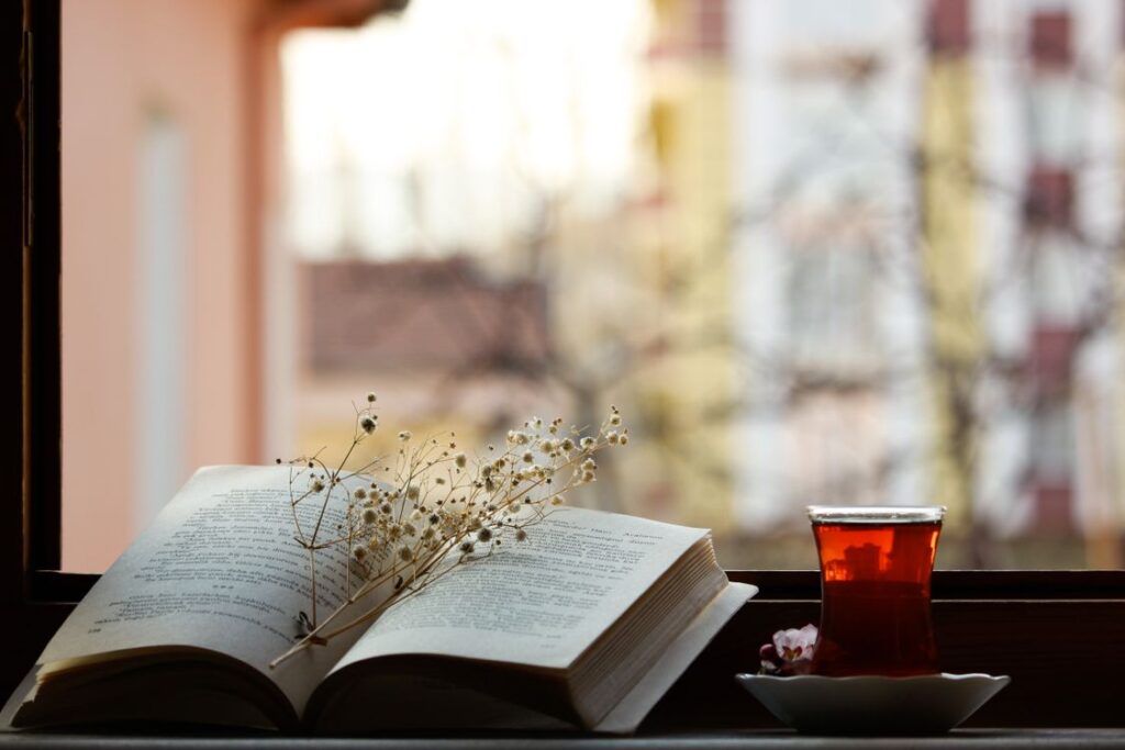 窓辺に開いた本と花、お茶のグラス