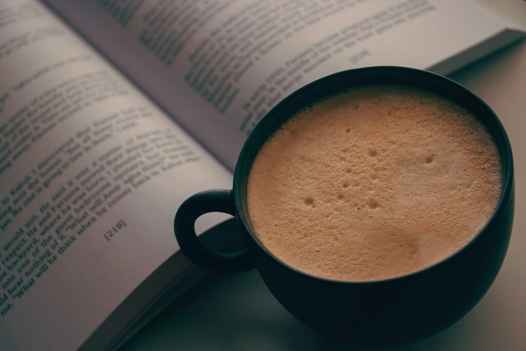 開いた本のそばにある黒いカップのコーヒー