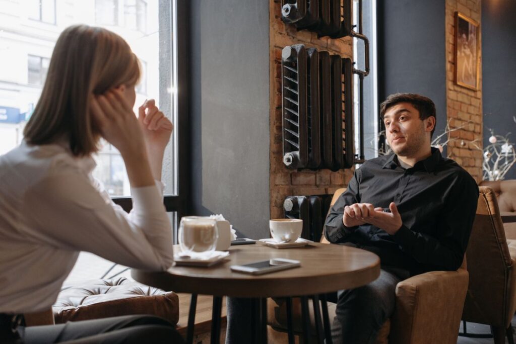 カフェのテーブルを挟んで飲み物を前に会話する二人