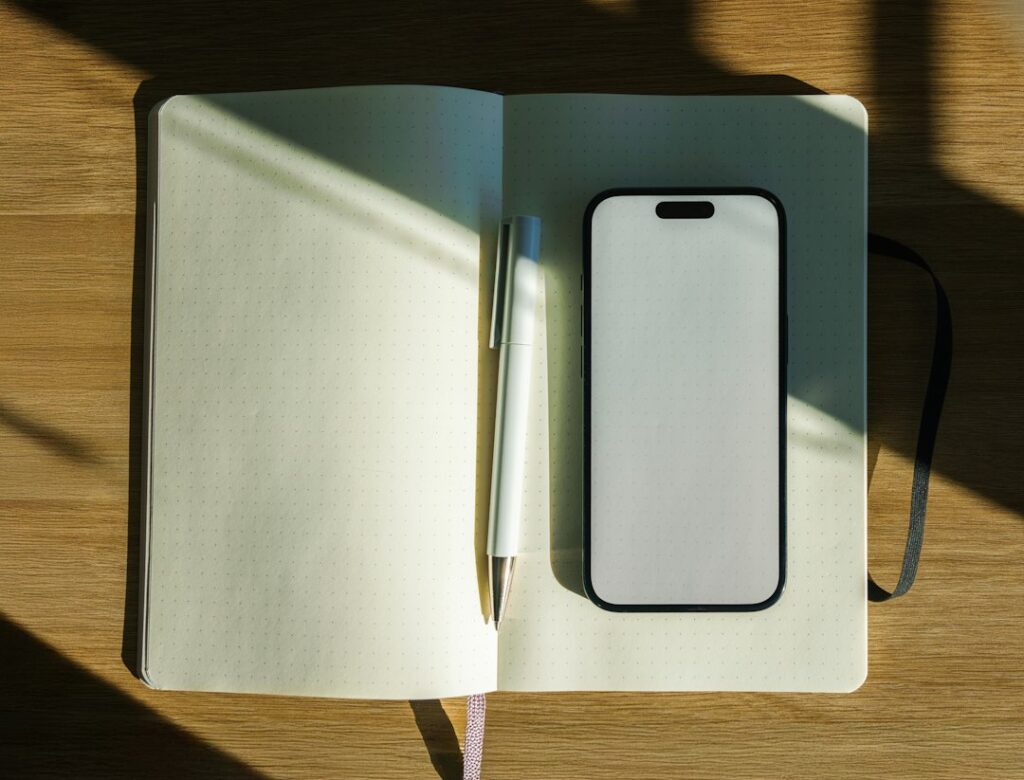 木の机に広げたノートとペン、白い画面のスマートフォン