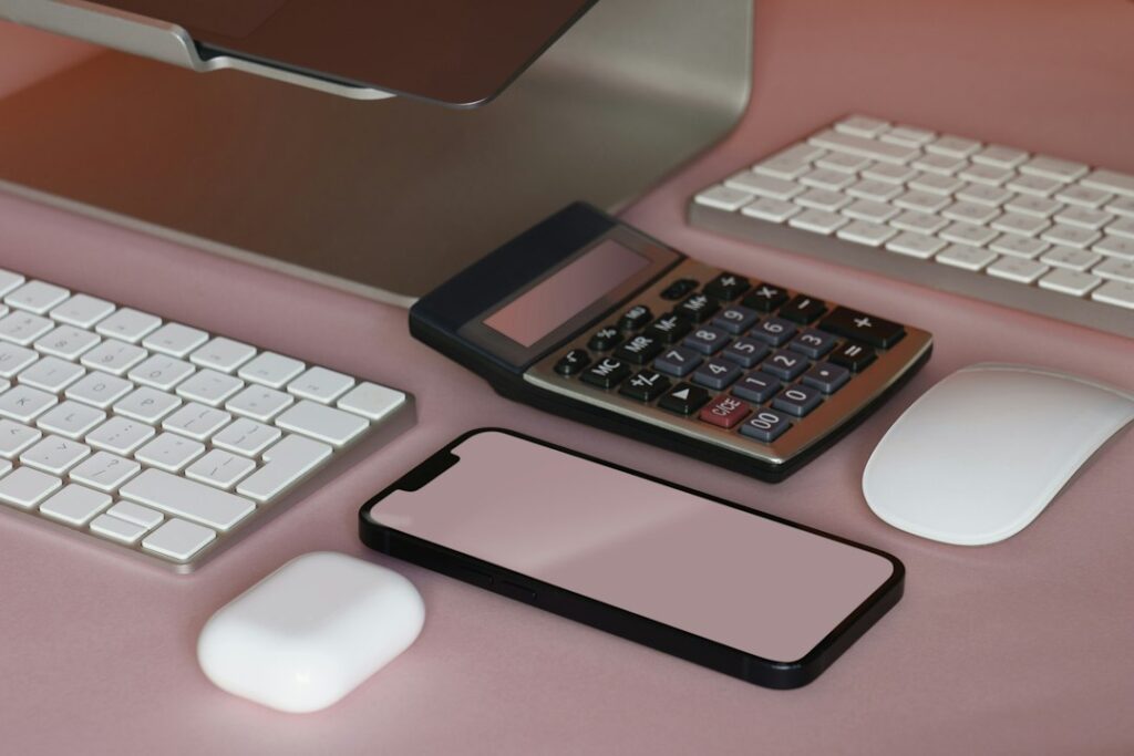 ピンク色の机に置かれた電卓、画面が空白のスマートフォンとキーボード